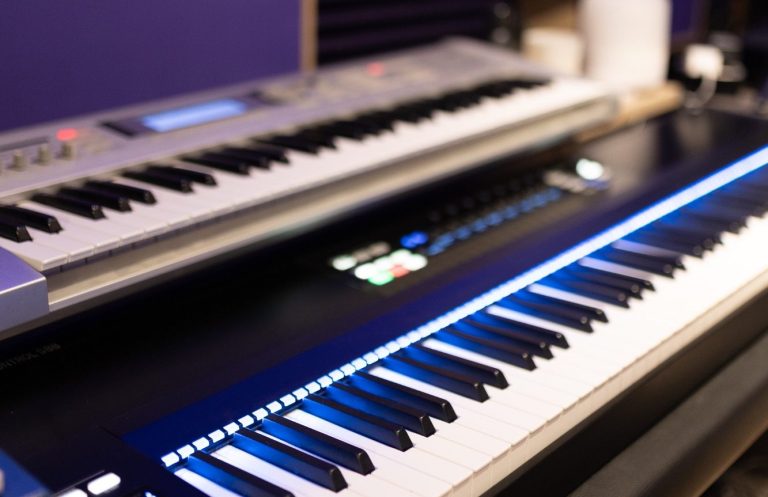 Tonstudio mit Synthesizer, Piano, blauen Wänden, Akustikpaneelen und Mikrofonen in der Ecke.
