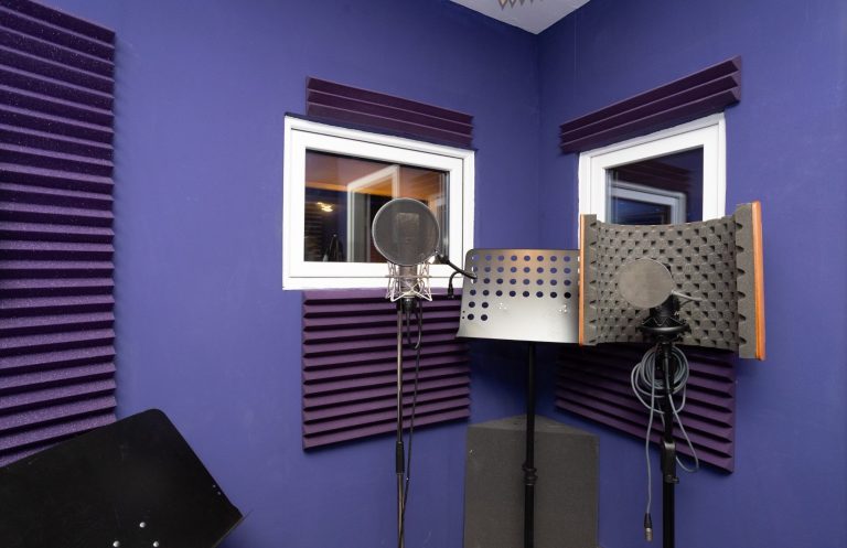 Tonstudio mit blauen Wänden, Akustikpaneelen und Mikrofonen in der Ecke.