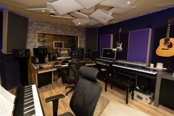 Moderne Musikproduktionsumgebung mit Instrumenten, Mischpult und Schreibtischstuhl.